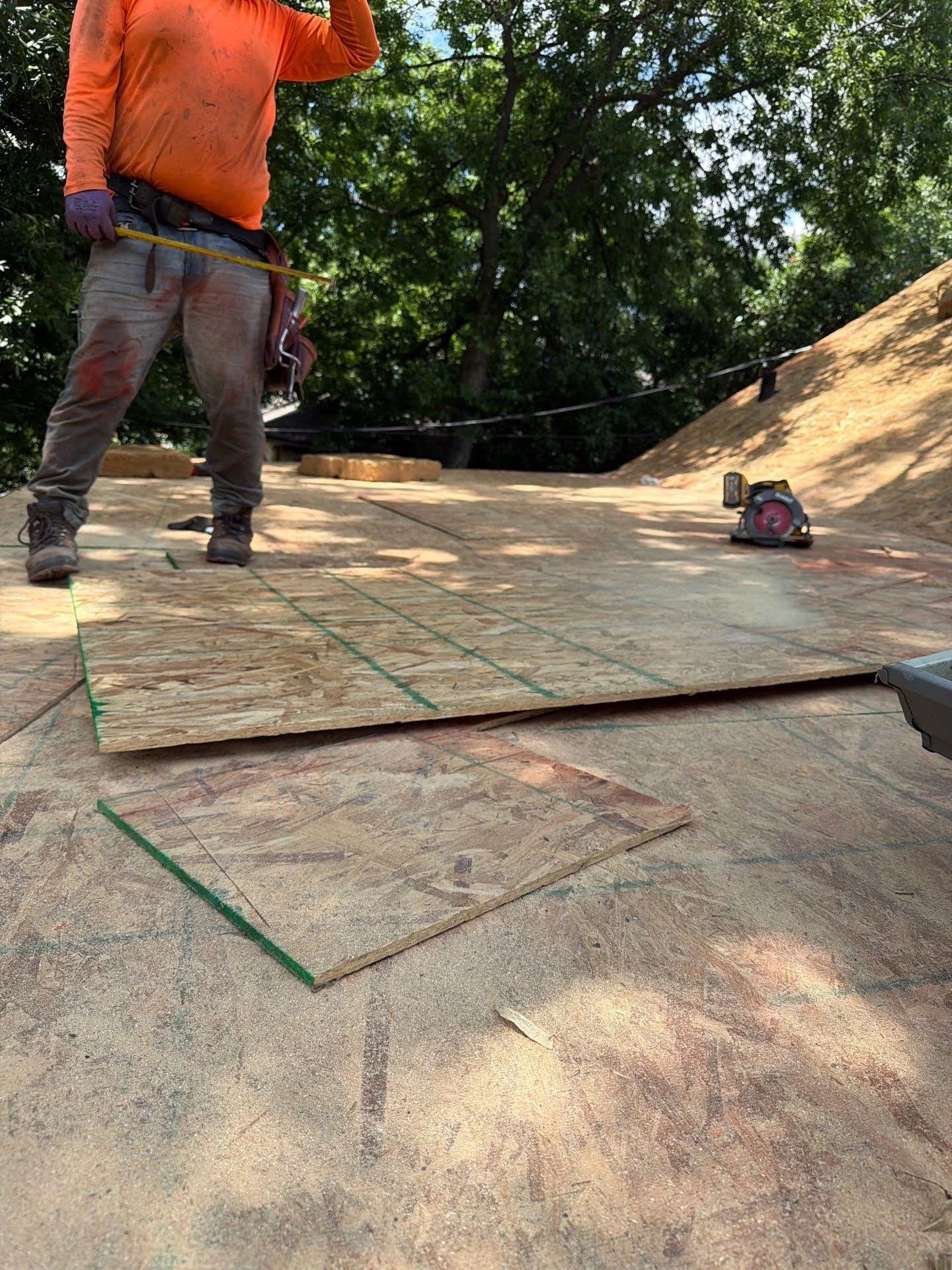 Roofer measuring and marking plywood decking with chalk lines on residential roof