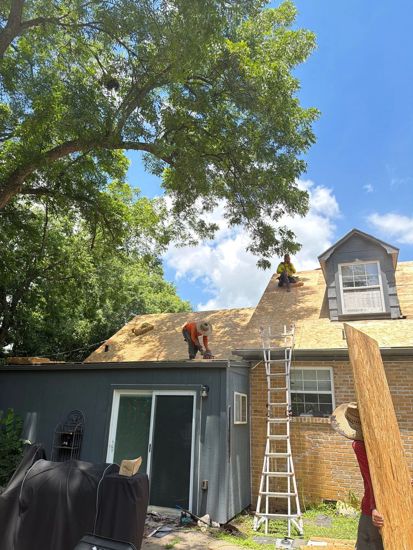 Roofer in orange vest installing new shingles on pitched residential roof with dormer