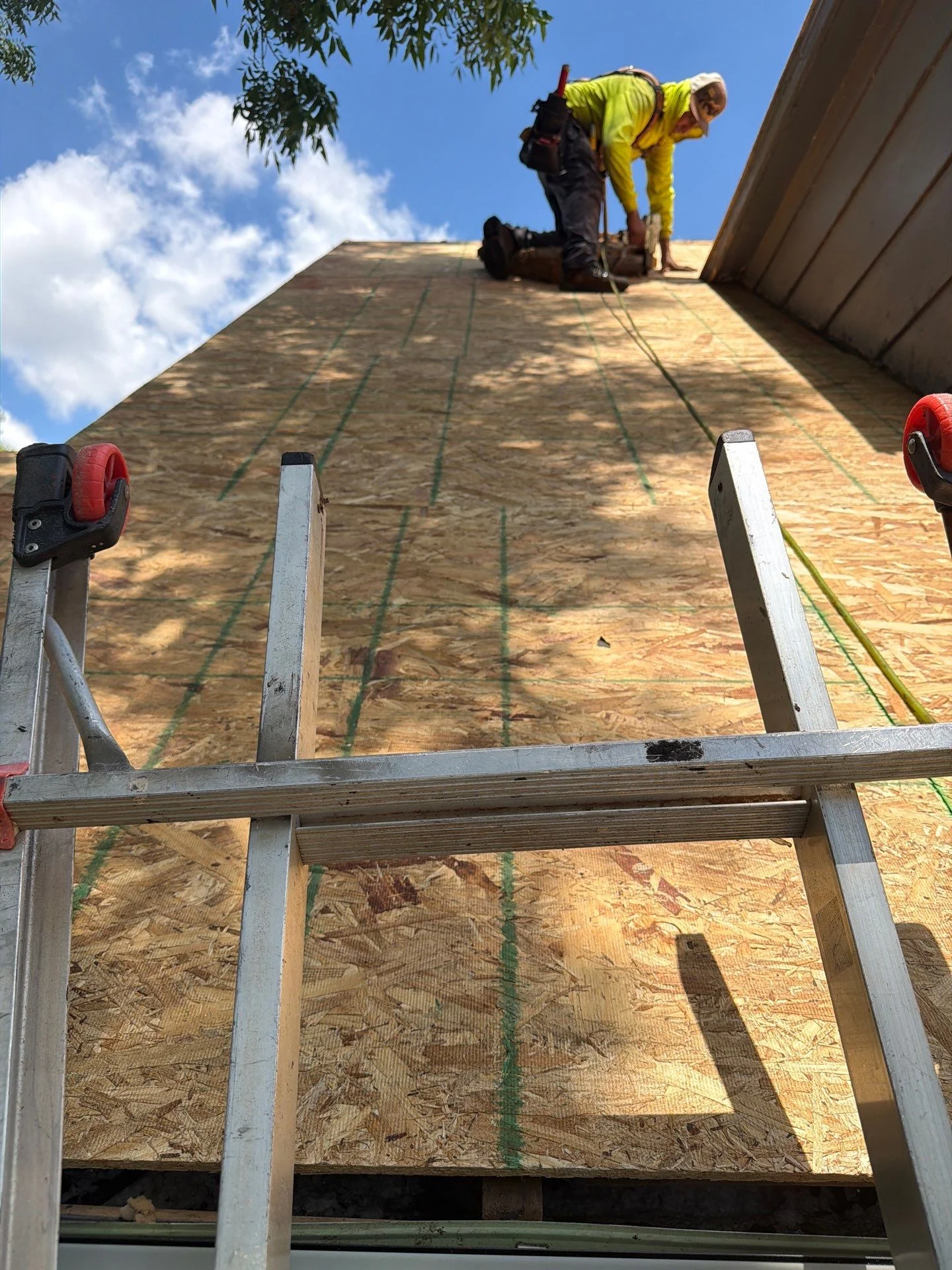 Roofer in yellow shirt installing OSB sheathing on residential roof frame with safety equipment
